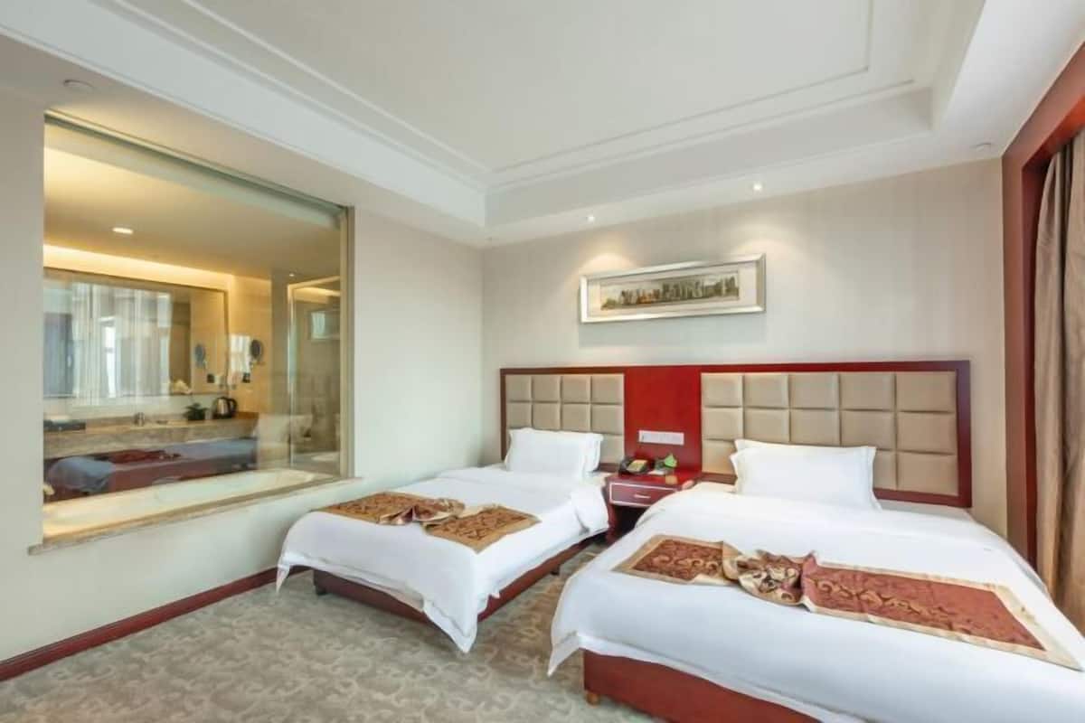 A hotel room with two beds, a large mirror, a framed picture on the wall, and a red accent wall.
