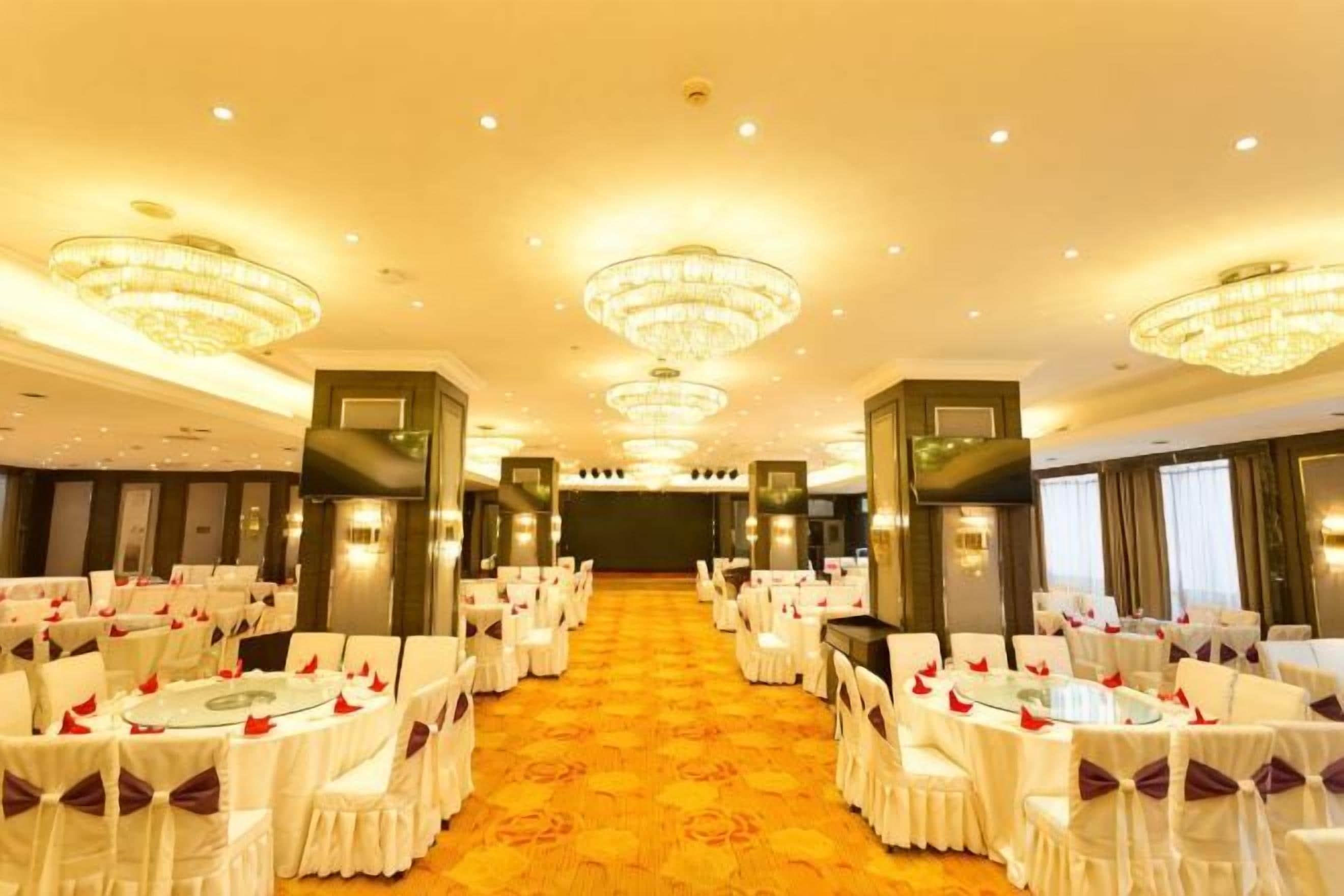 A banquet hall with round tables, chairs, chandeliers, and a carpeted floor.