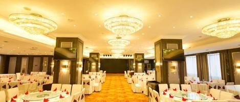 A banquet hall with round tables, chairs, chandeliers, and a carpeted floor.