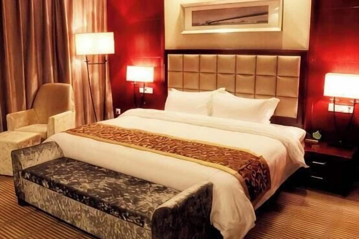A hotel room with a large bed, a chair, a bench, and two bedside lamps.
