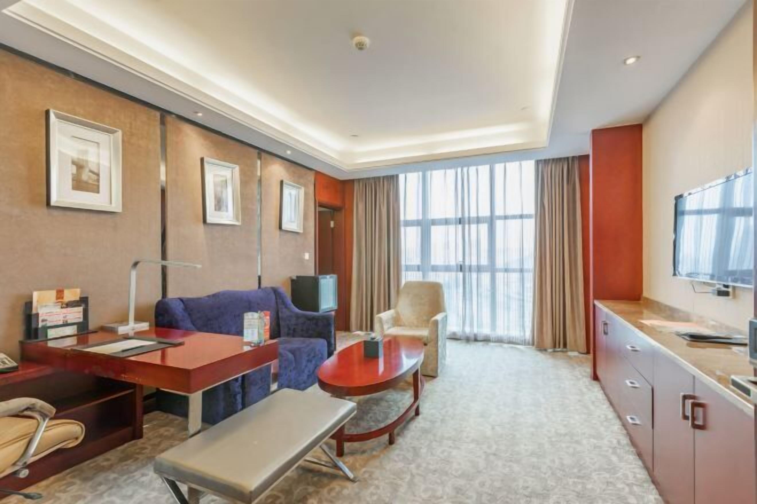 A hotel room with a sofa, armchair, desk, and television.