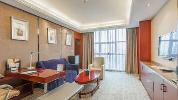 A hotel room with a sofa, armchair, desk, and television.