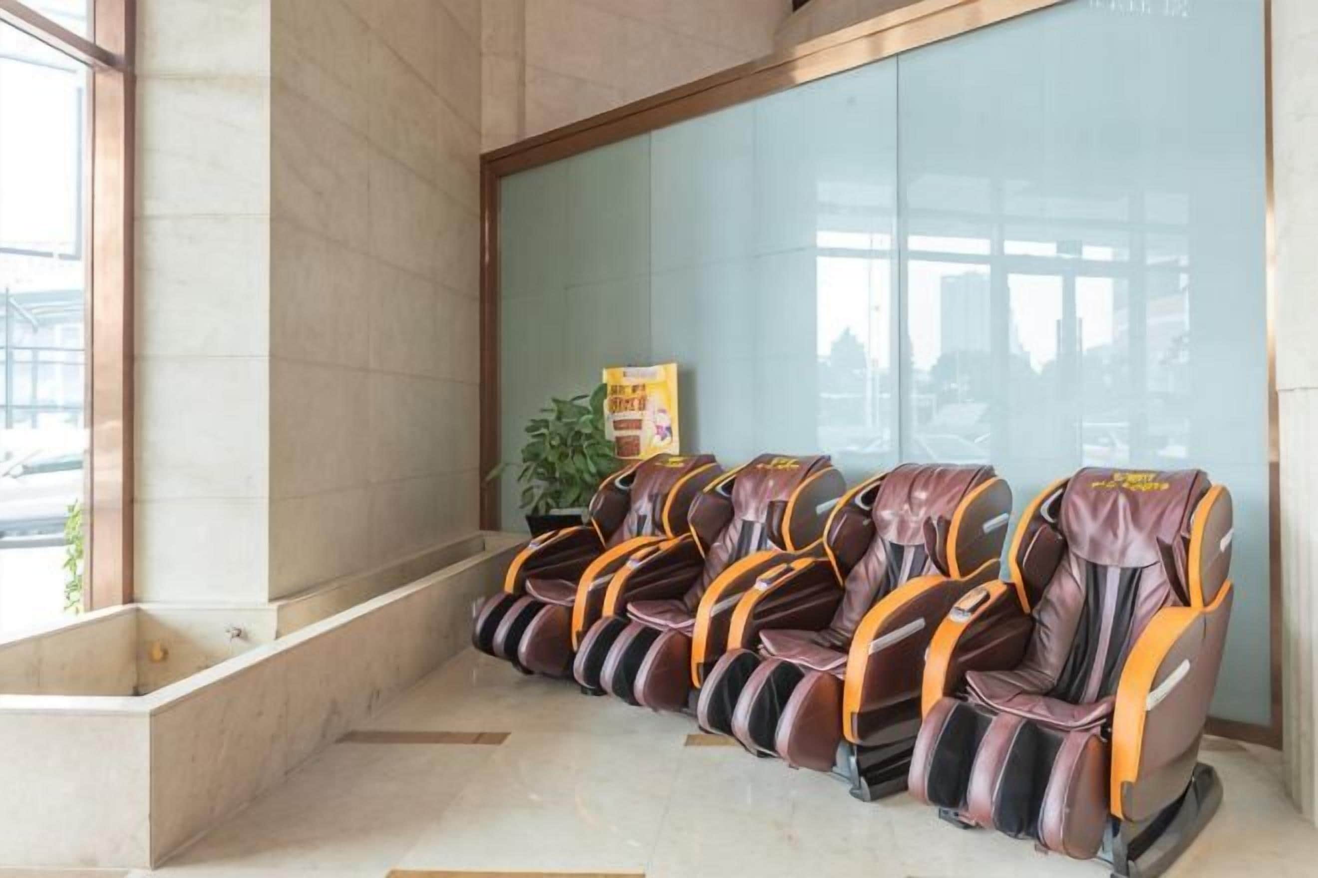 A row of massage chairs in a waiting area with a glass wall and a plant.
