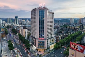 A high-rise building with a prominent sign at the top, surrounded by a cityscape with various other buildings and a busy road. - Guomao Hotel (Yichang)