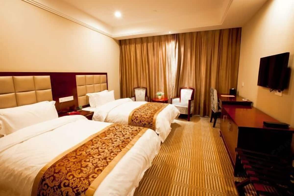 A hotel room with two beds, a desk, a television, and a large window with curtains.