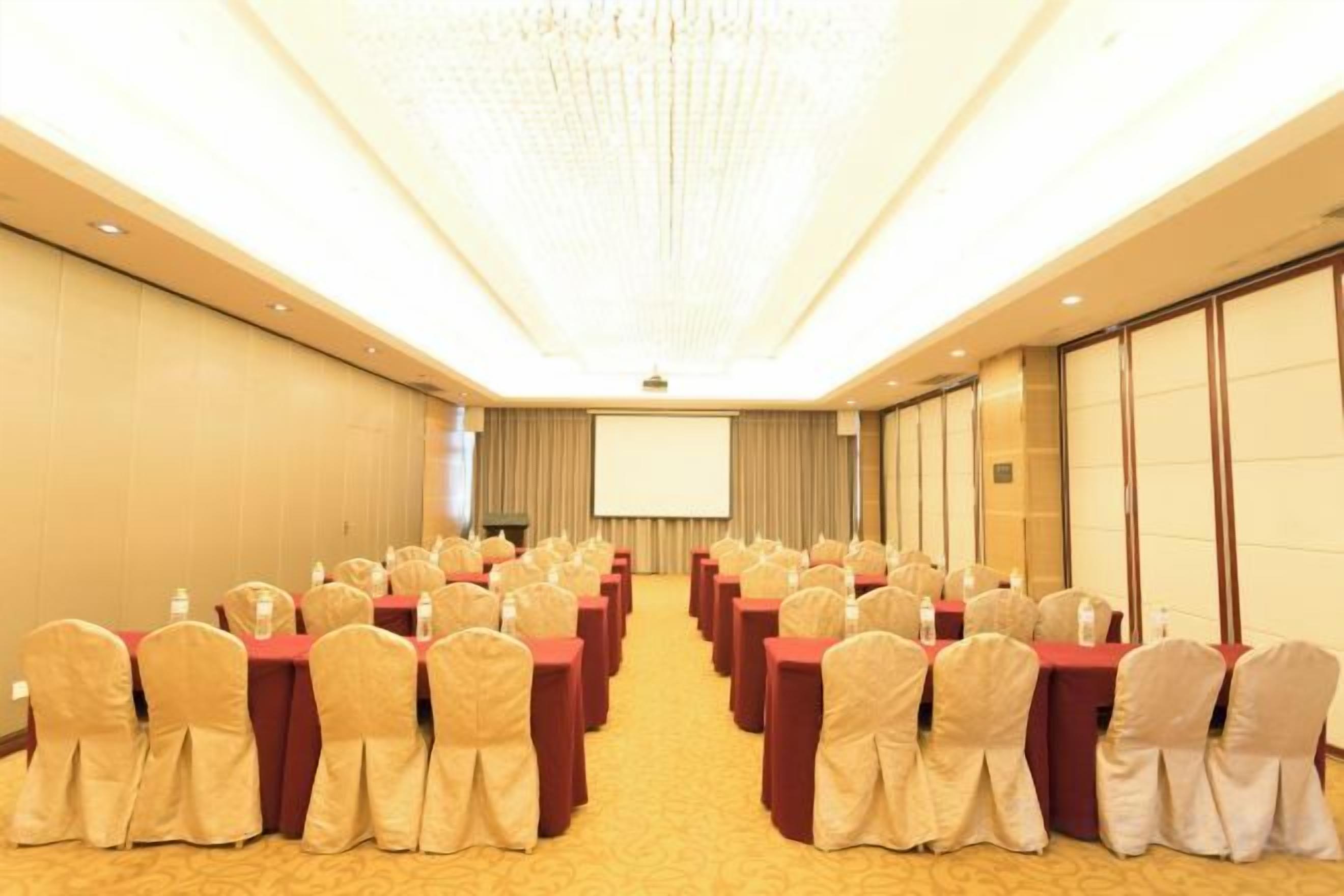 A conference room with rows of tables and chairs, a projector screen, and a carpeted floor.