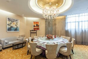Uma área de refeições com uma mesa redonda, cadeiras, um lustre, obras de arte nas paredes e um sofá.