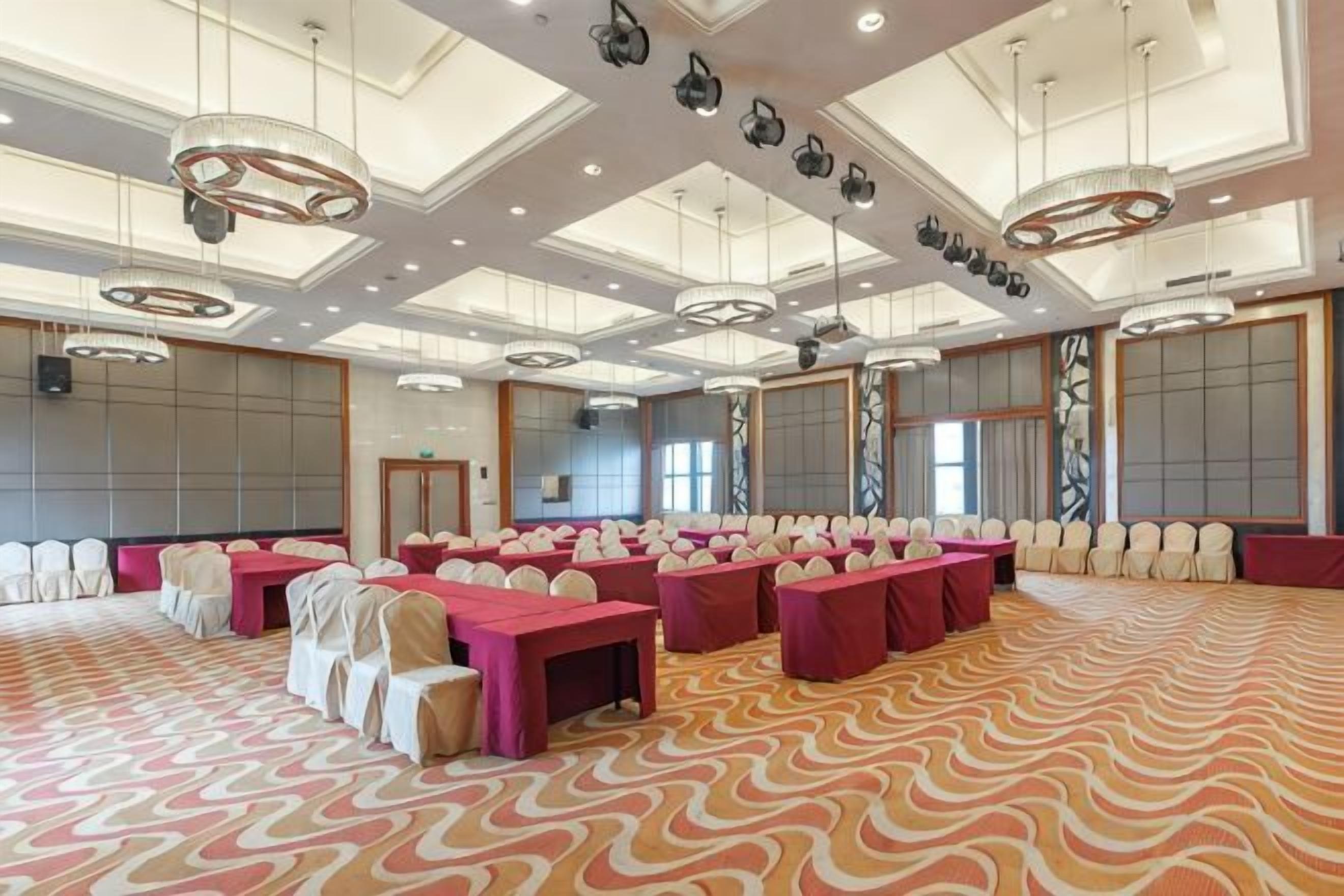 A large conference room with multiple tables and chairs, high ceilings with recessed lighting, and a patterned carpet.