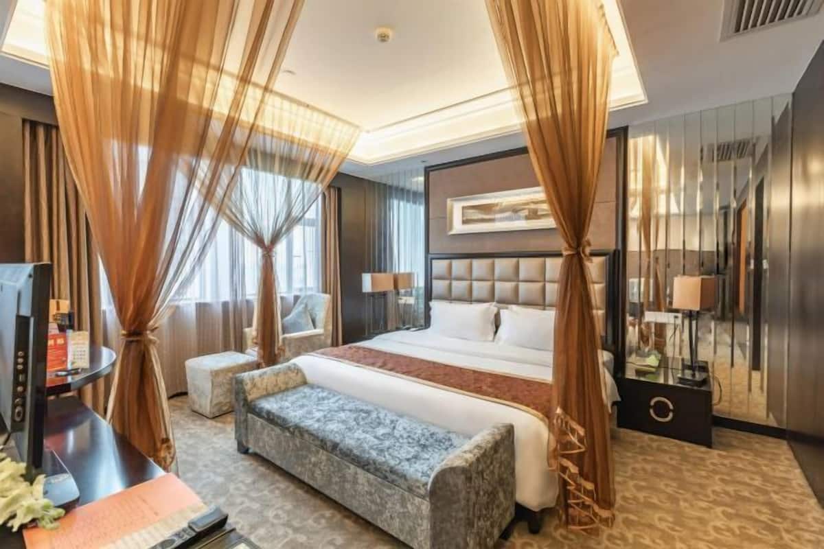 A hotel room with a large bed, a desk with a computer, a bench, and a TV.