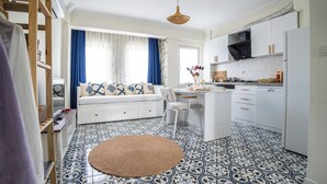 Un espace de vie compact comprenant un coin cuisine, un canapé agrémenté de coussins à motifs, un coin repas et un sol à motifs.