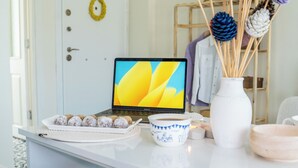 Un ordinateur portable sur un bureau blanc, avec une assiette de biscuits, une tasse et un vase décoratif.