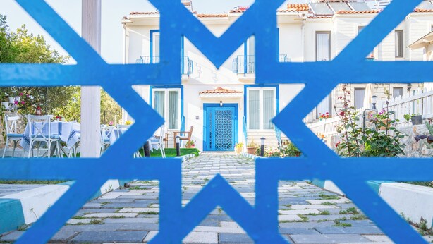Une cour avec un portail bleu qui mène à un bâtiment doté d’un toit en tuiles et d’une porte bleue.