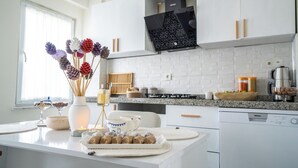 Une cuisine moderne avec des armoires blanches, un comptoir en granit et une cuisinière encastrée. On y trouve également des pommes de pin décoratives et un vase rempli de fleurs séchées sur le comptoir.