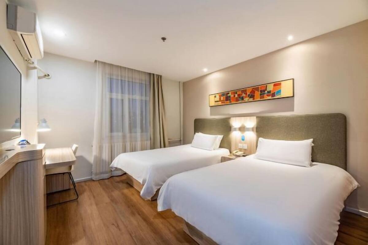A hotel room with two beds, a desk, a chair, a TV, and a painting on the wall.