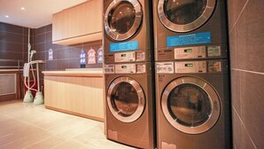 A modern laundry facility with two stacked front-loading washing machines and a wooden counter. - HanTing Hotel (Jilin Street Railway Station) (Jilin City)