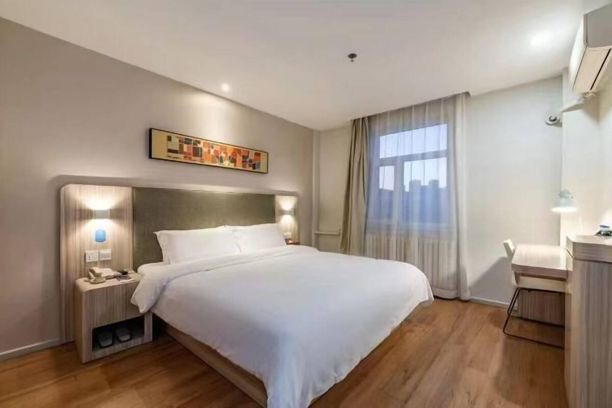 A hotel room with a bed, bedside lamps, a desk, and a window with curtains.