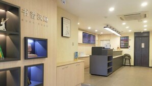 A reception area with a counter, shelves with books, a framed picture, and a staircase leading to another level. - HanTing Hotel (Jilin Street Railway Station) (Jilin City)