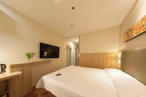Una habitación de hotel con una cama, un escritorio con una planta, un televisor de pantalla plana y un cuadro en la pared.