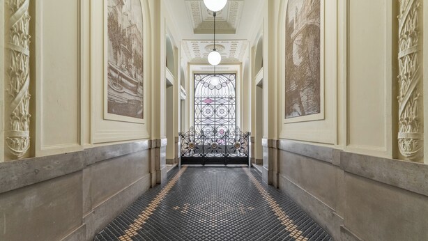 A corridor with a patterned floor, ornate wall decorations, and a large window with a metal gate. - Montello Suites Foresteria Lombarda (Milan)