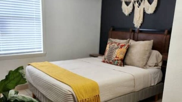 Un dormitorio con una cama, cabecera de madera, un tapiz de macramé y un sofá de cuero marrón.