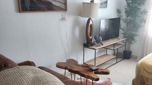 Una sala de estar con un sofá de cuero marrón, una mesa de centro de madera, un televisor sobre un mueble bajo y dos cuadros en la pared.