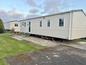 A mobile home with a covered patio, a small attached utility building, and a grassy area in the foreground. - Immaculate 3-bed Static Caravan in Skegness (Skegness)