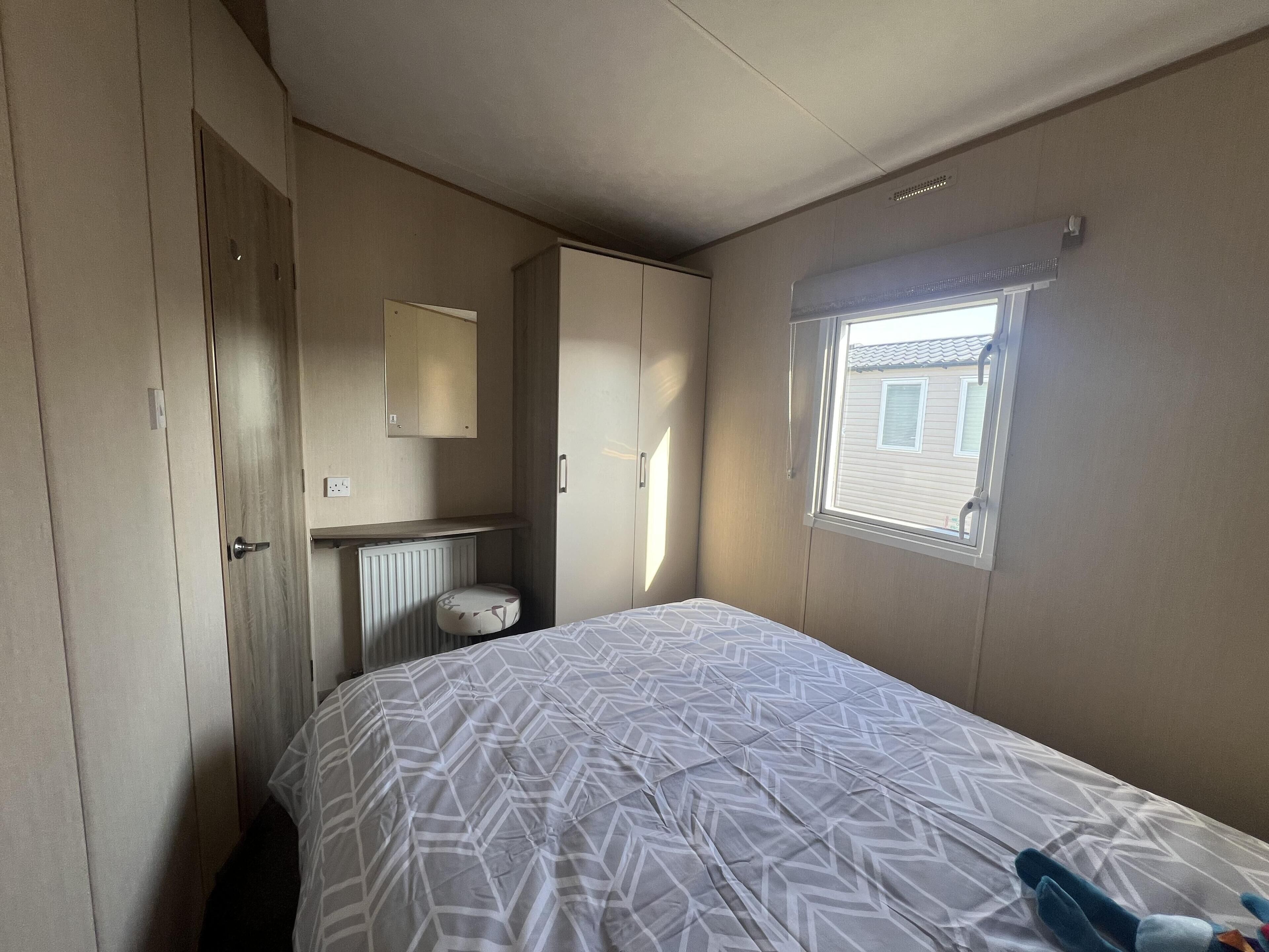 A bedroom with a bed, a radiator, a window, and a wardrobe.