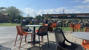 An outdoor patio with round tables and chairs, a wooden deck, and a covered seating area with a TV screen. - Immaculate 3-bed Static Caravan in Skegness (Skegness)