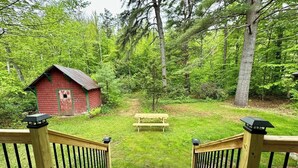 Eine Holzterrasse führt zu einer grünen Wiese mit einem roten Gebäude und einem Picknicktisch.