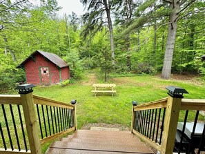 A wooden deck leading to a grassy area with a red building and a picnic table.