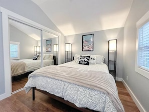 A bedroom with a large bed, a mirror, bedside lamps, and a window. - The Almost There | Conway NH (Conway)