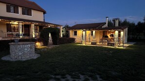 A two-story house with a stone facade, a patio with outdoor furniture, and a brick fireplace.