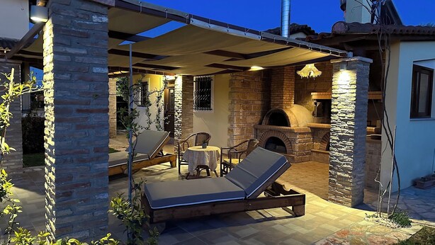 An outdoor patio with a stone fireplace, lounge chairs, and a table.