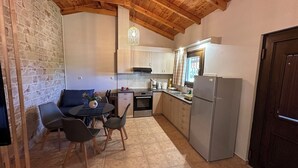 A compact kitchen with a dining area, stone wall, wooden ceiling, and a small table with chairs.