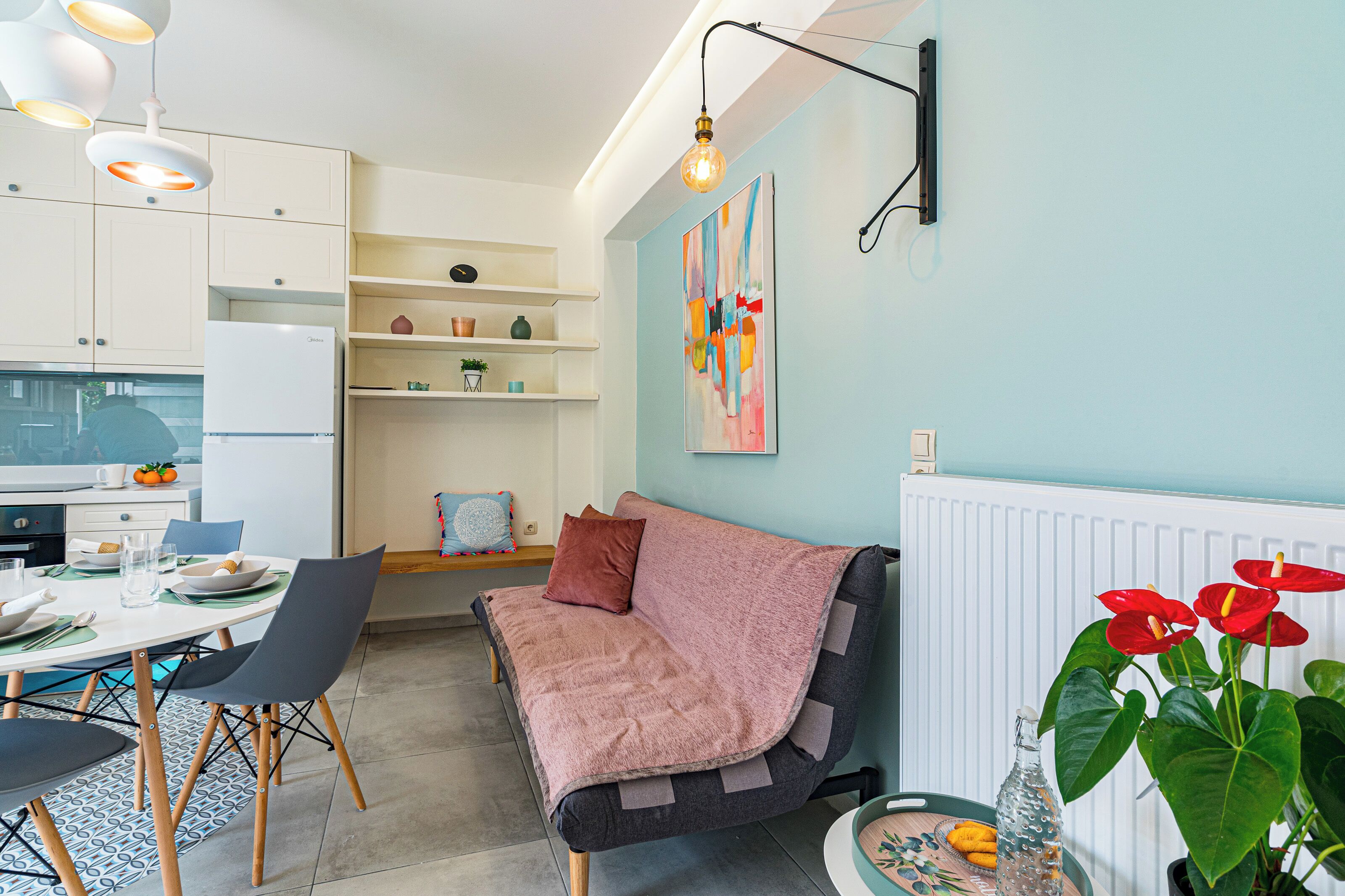 Eine moderne Küche mit weißen Schränken, einem Esstisch mit Stühlen und einem Sofa mit einer rosafarbenen Decke.
