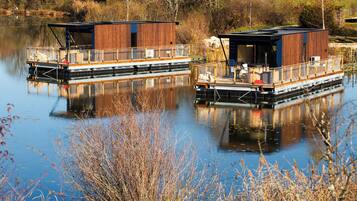 Two floating houses with wooden exteriors, each featuring a deck with seating and a railing.