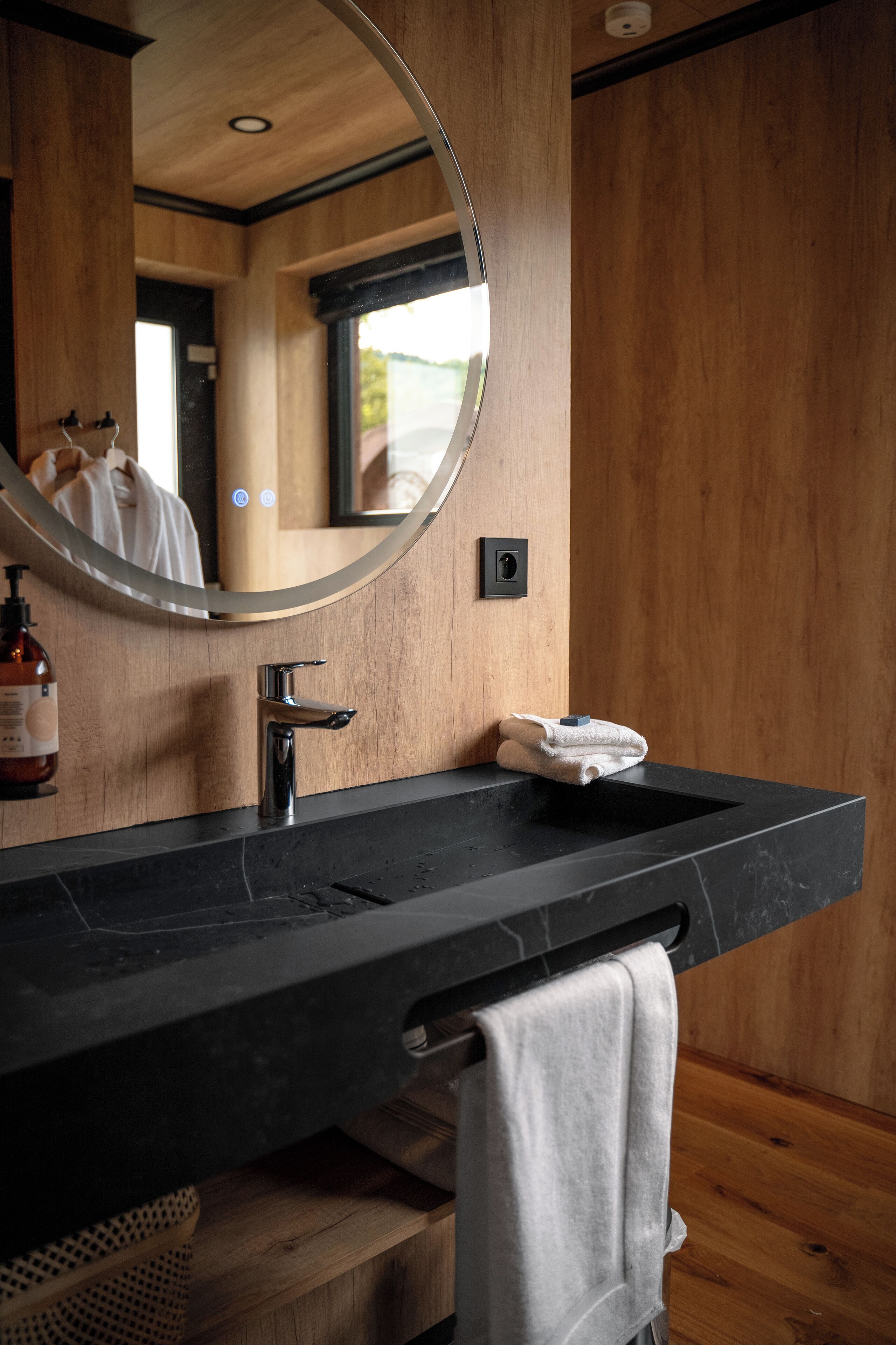 A modern bathroom with a black marble sink, a round mirror, and wooden paneling.