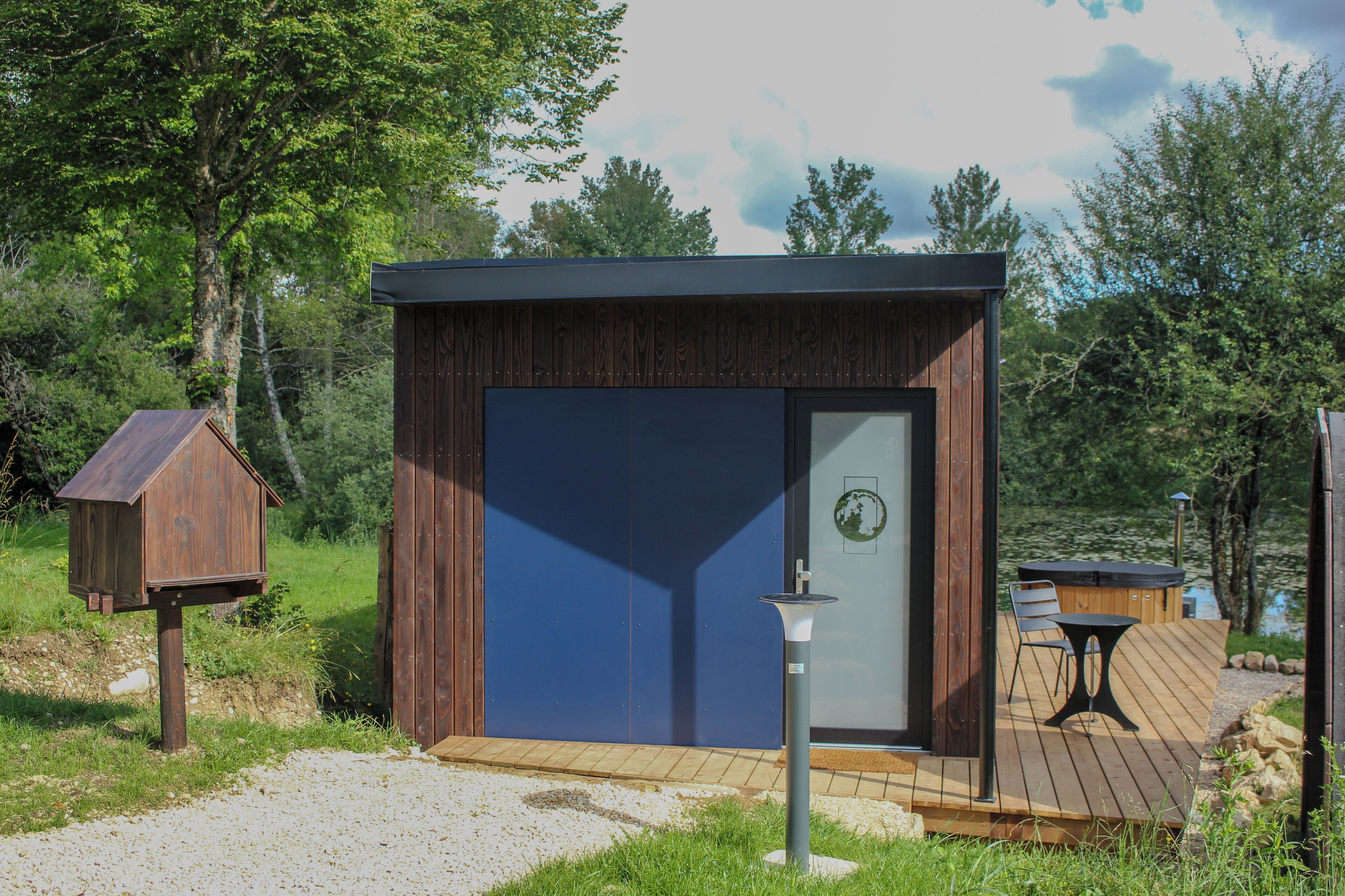 A small wooden cabin with a dark blue door, a wooden deck, and a hot tub.