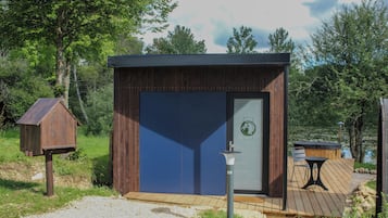 A small wooden cabin with a dark blue door, a wooden deck, and a hot tub.