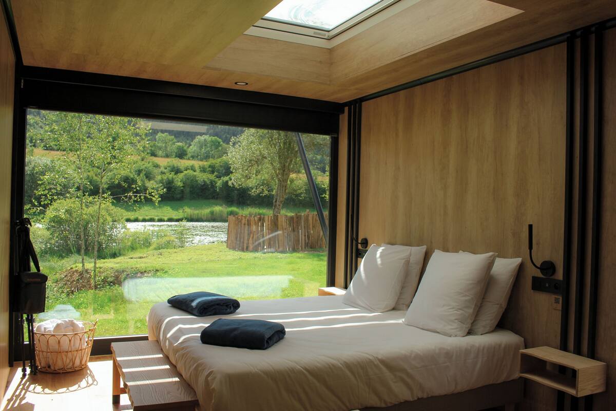A bedroom with a large window, a bed with white linens, and a wooden headboard.