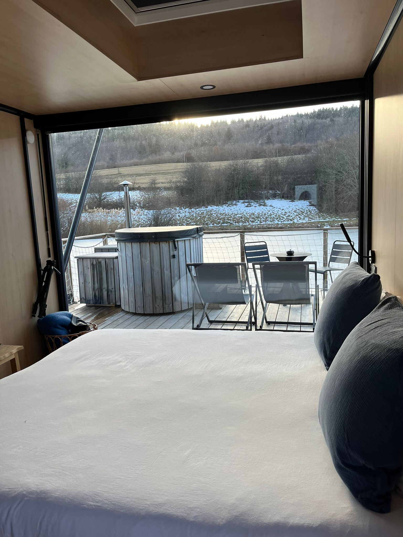 A bedroom with a large bed, a view of a snowy landscape, a hot tub, and outdoor seating.