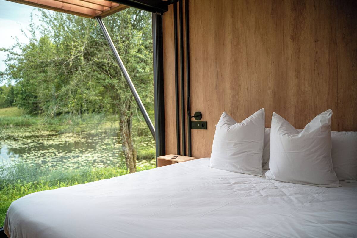 A bedroom with a large window overlooking a natural landscape.