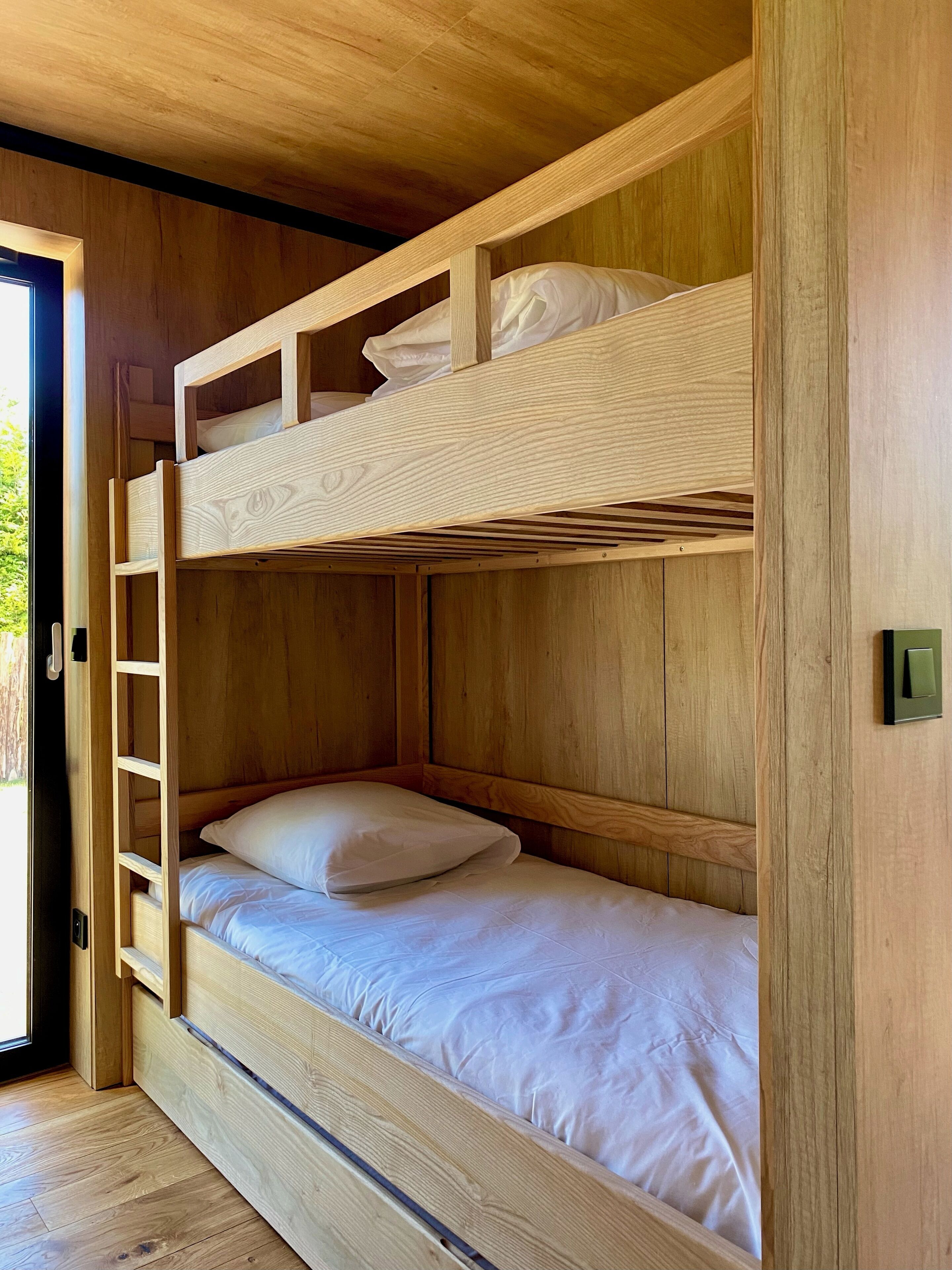 A bunk bed with a ladder, wooden walls, and a door leading outside.