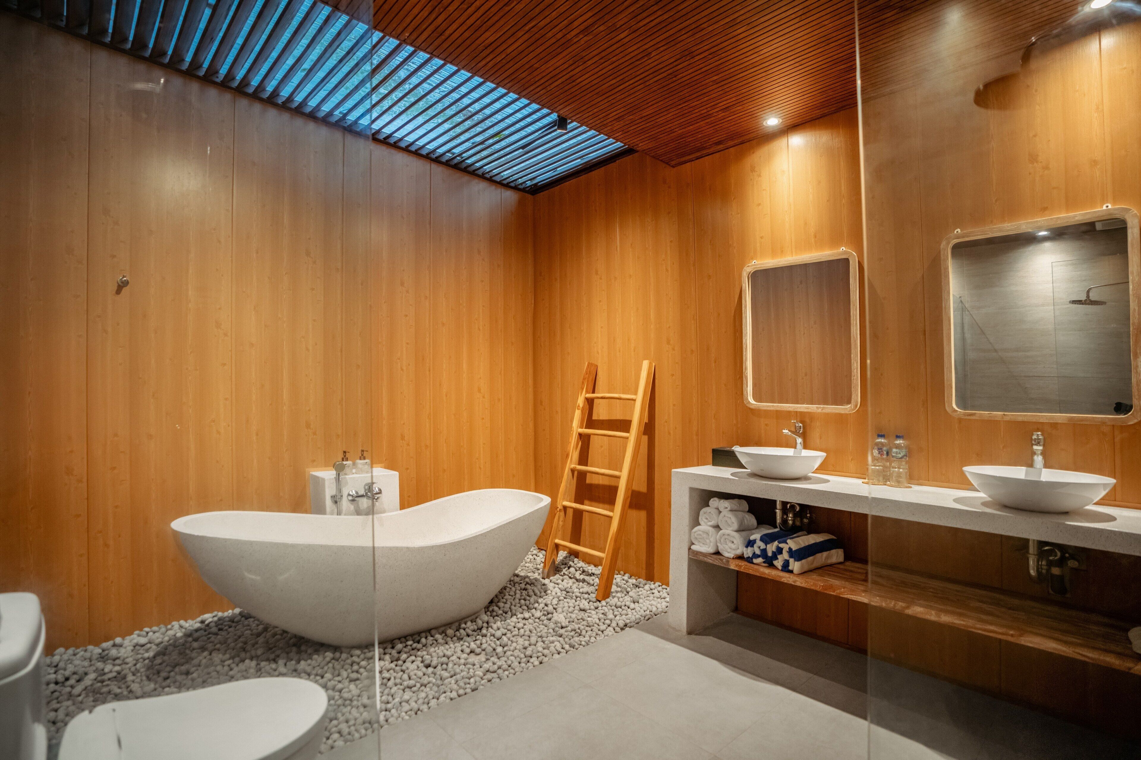 Une salle de bain moderne avec des murs en bois, une baignoire sur pieds, une échelle en bois et un meuble-lavabo avec deux vasques.