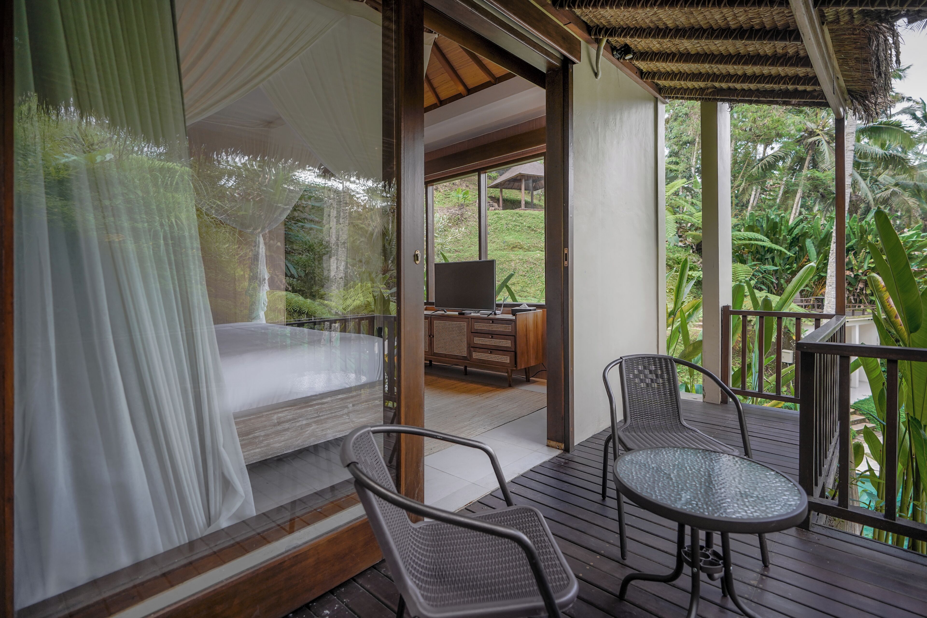 A bedroom with a bed, a TV, and a balcony with chairs and a table.