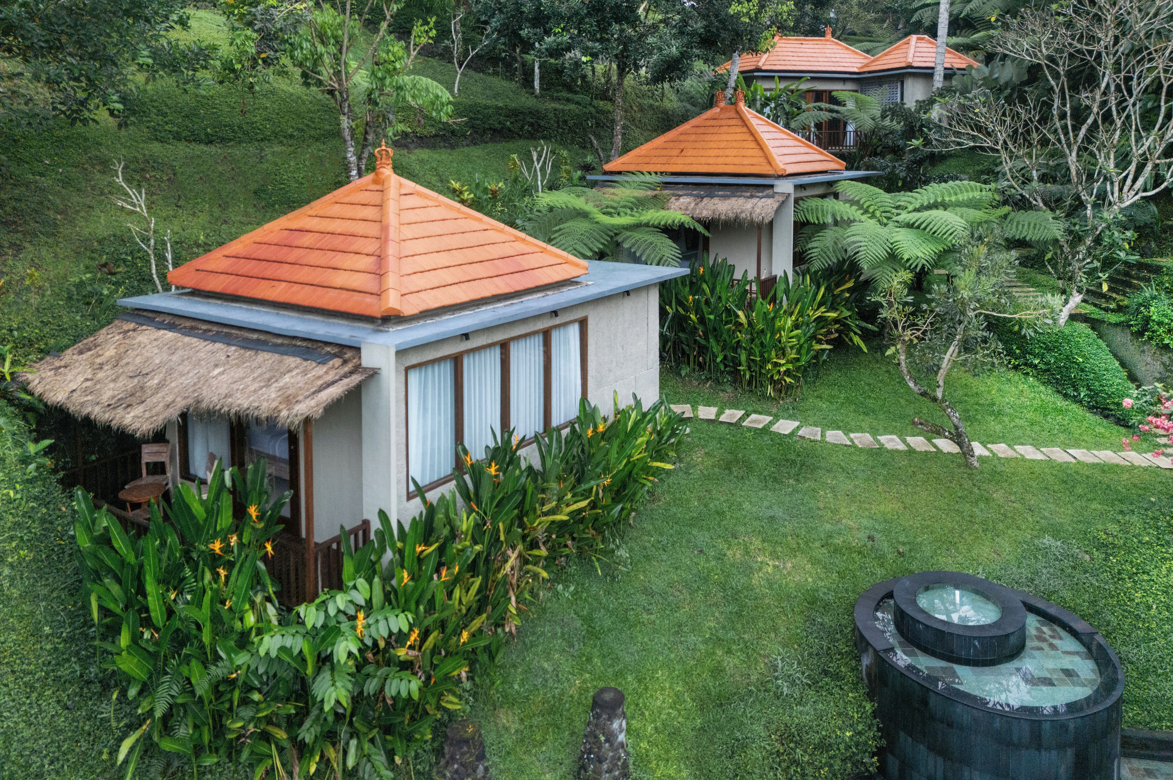 A bungalow with a thatched roof, surrounded by lush greenery and a hot tub.