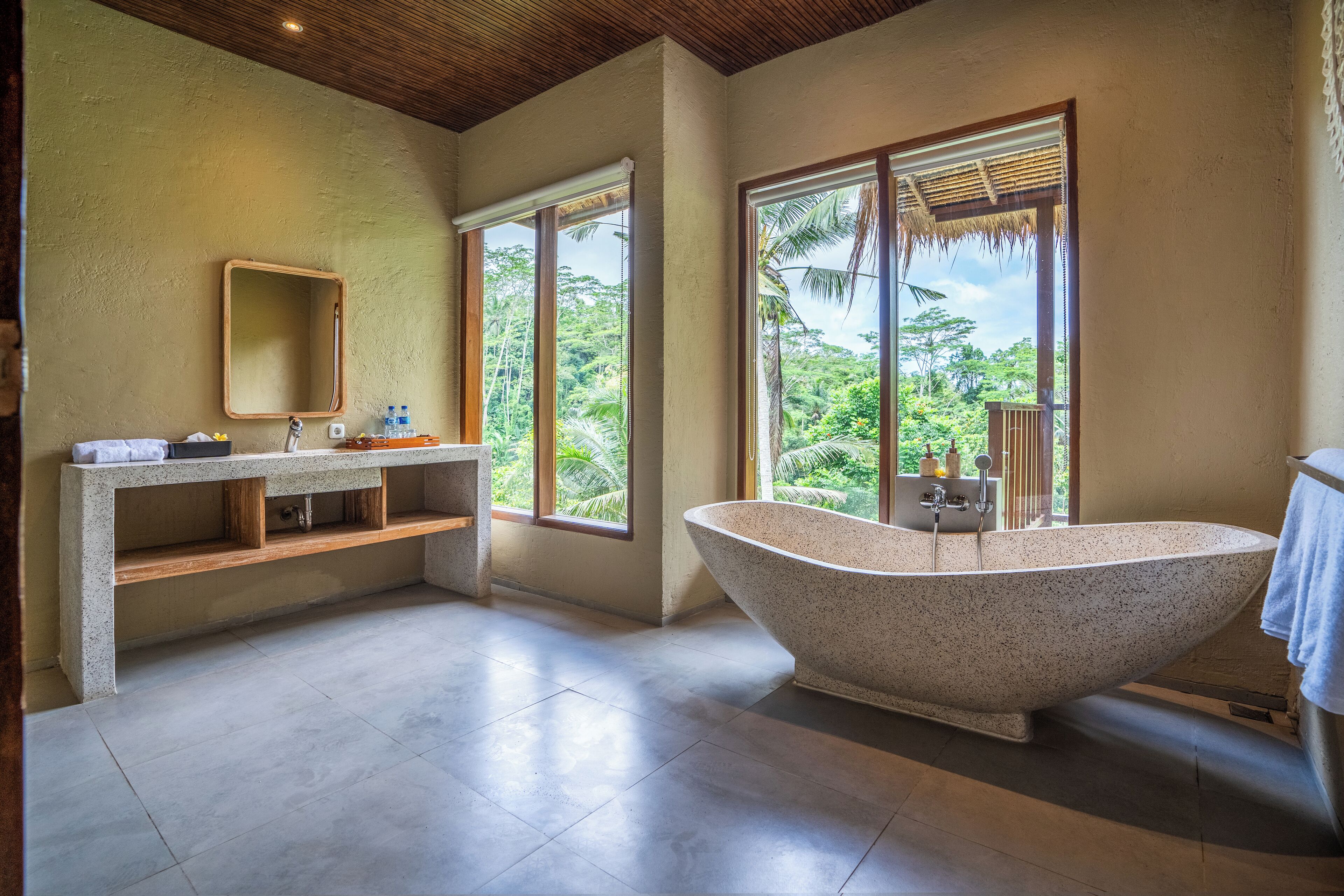 A modern bathroom with a freestanding bathtub, a vanity with a mirror, and large windows offering a view of lush greenery.