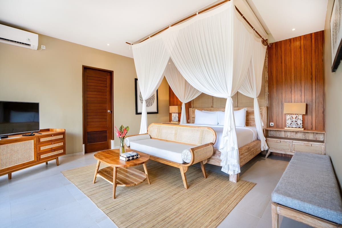 Un dormitorio con cama con dosel, un sofá, un televisor y un aparador de madera.