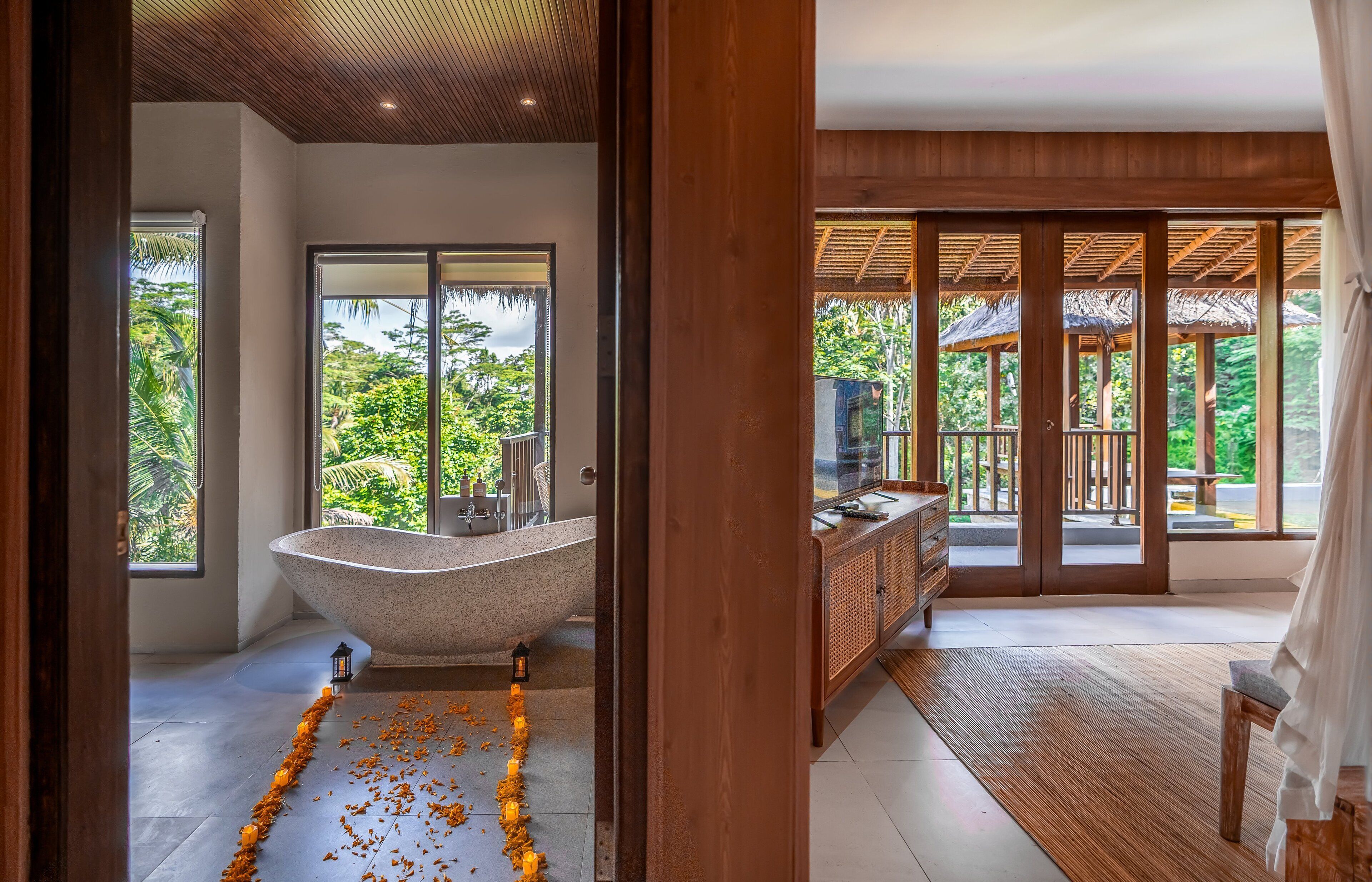 A bathroom with a freestanding bathtub, a vanity, and a large window offering a view of lush greenery.