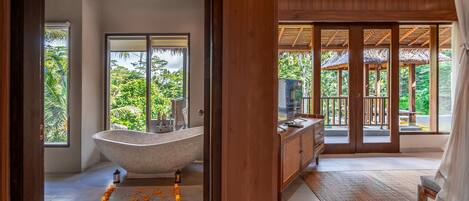 A bathroom with a freestanding bathtub, a vanity, and a large window offering a view of lush greenery.